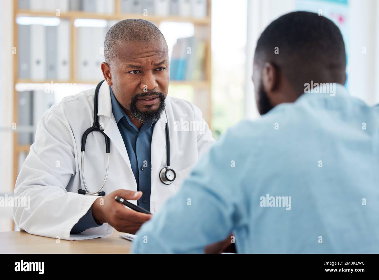 Serious doctor having a consult with a patient. Medical doctor talking to a patient about his results. African american patient speaking to his doctor Stock Photo
