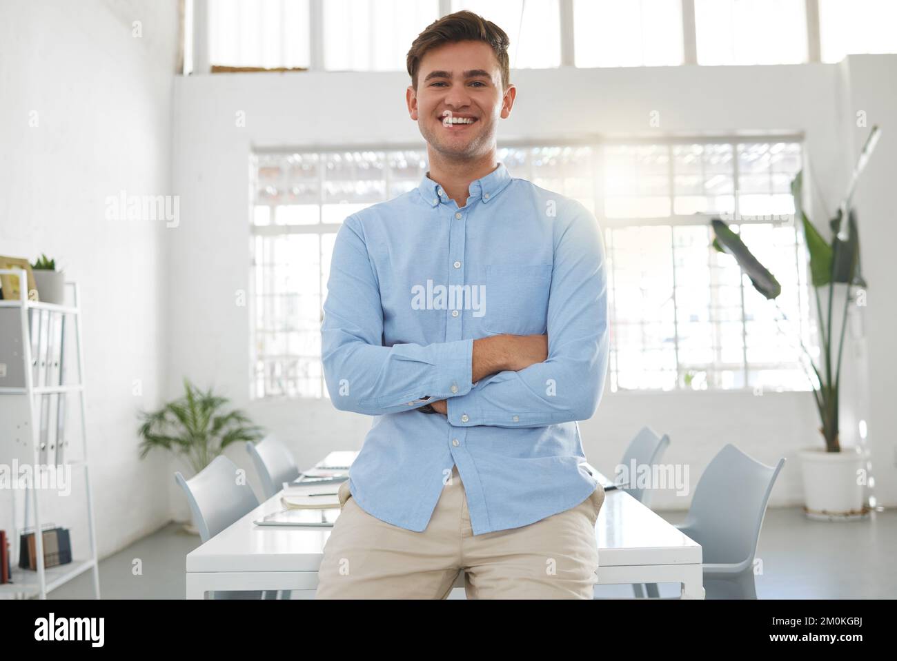Young happy caucasian businessman standing with his arms crossed while in an office alone. One confident male boss standing at work Stock Photo