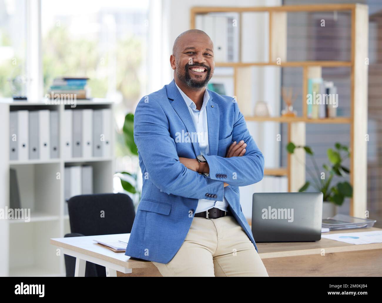 Success, corporate leadership and portrait of black man sitting on desk in modern office for startup. Management, marketing ceo and happy male Stock Photo