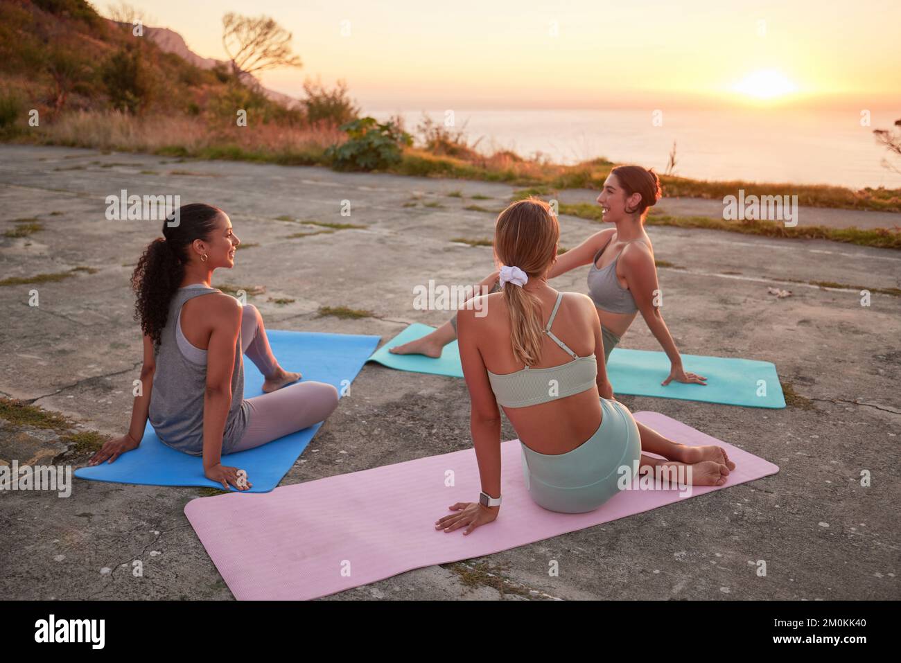 Full length of yoga women bonding, sitting together on mats after outdoor practice in remote nature. Diverse group of young active smiling friends at Stock Photo