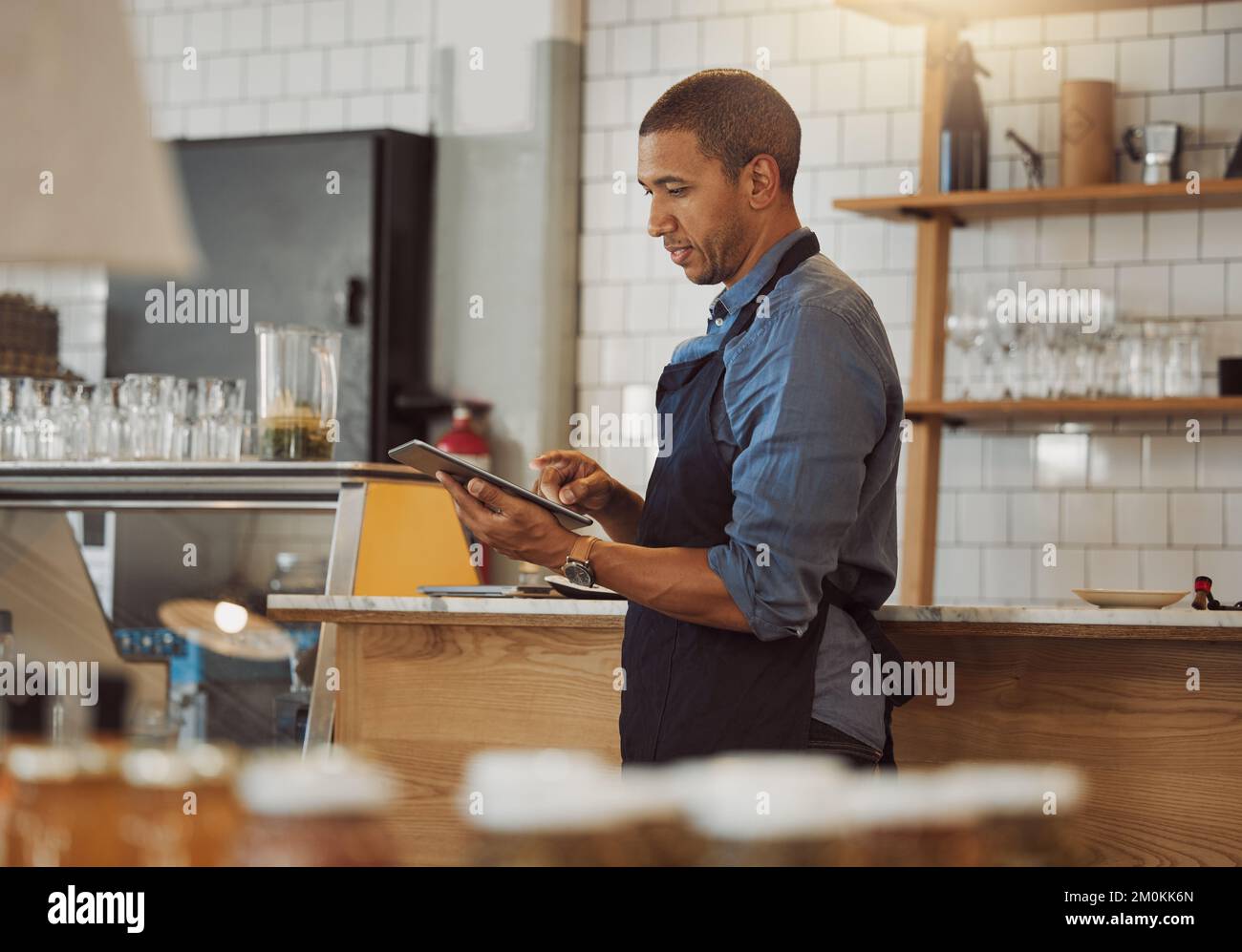 Mixed race businessman ordering stock on his digital tablet. Boss using a wireless device in his restaurant. Barista placing an online order on an app Stock Photo