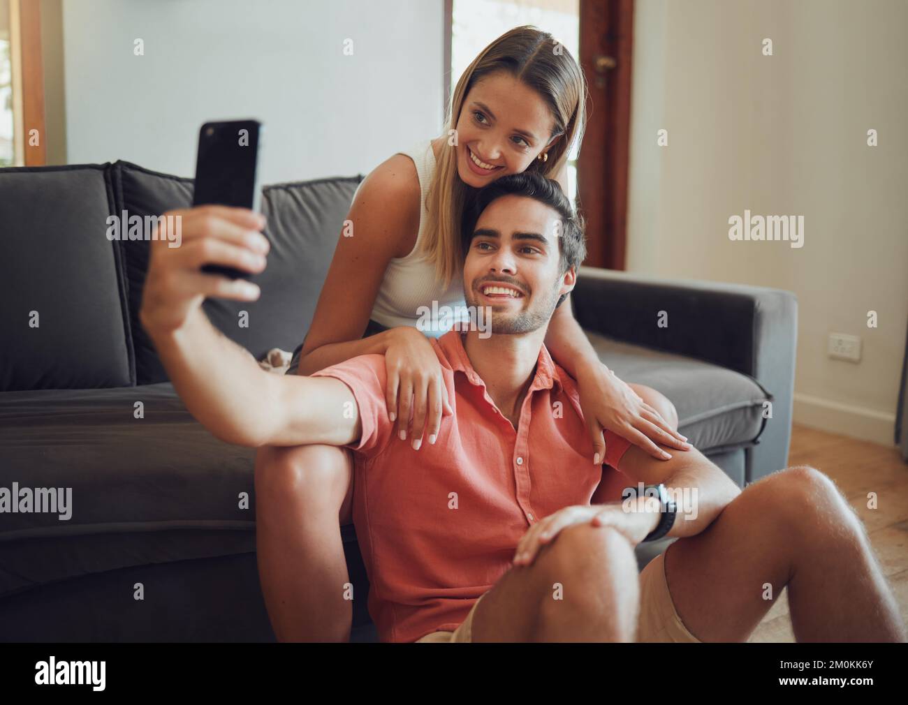 Happy young caucasian couple sitting together and taking selfie with smartphone. Young man holding mobile phone to take picture while sitting between Stock Photo