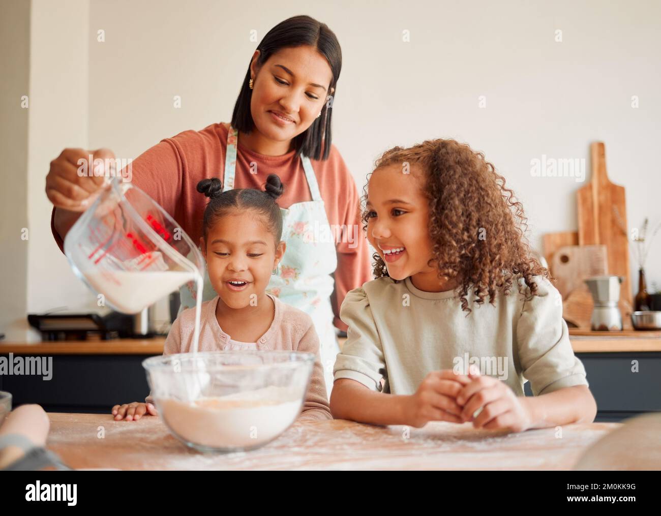 Females only, happy mixed race family of three cooking in a messy kitchen together. Loving black single parent bonding with her daughters while Stock Photo
