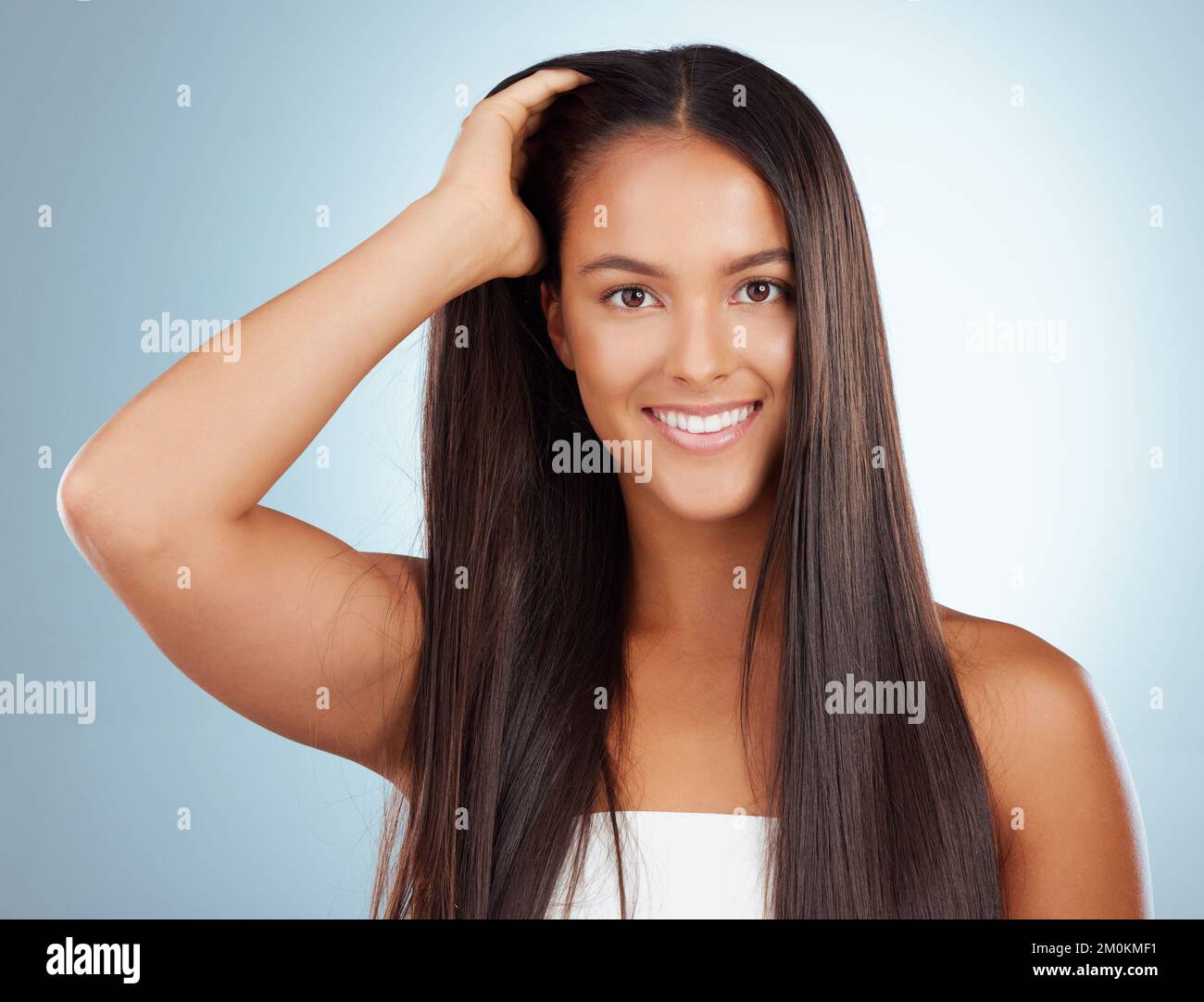 Portrait of a hispanic brunette woman with long lush beautiful hair smiling and posing against a grey studio background. Mixed race female standing Stock Photo