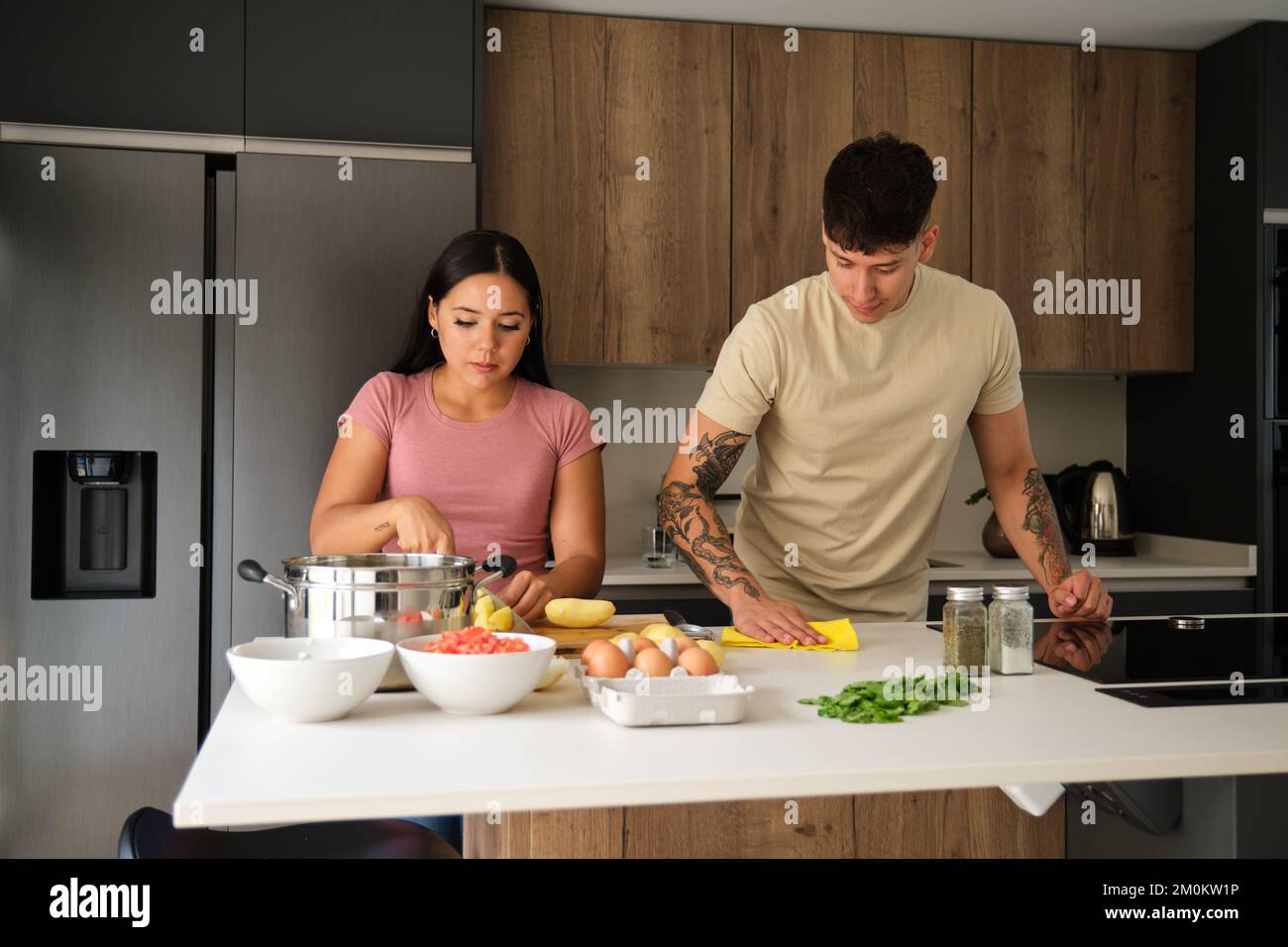 Two young latin people peeling potatoes and cleaning kitchen counter at kitchen. Stock Photo