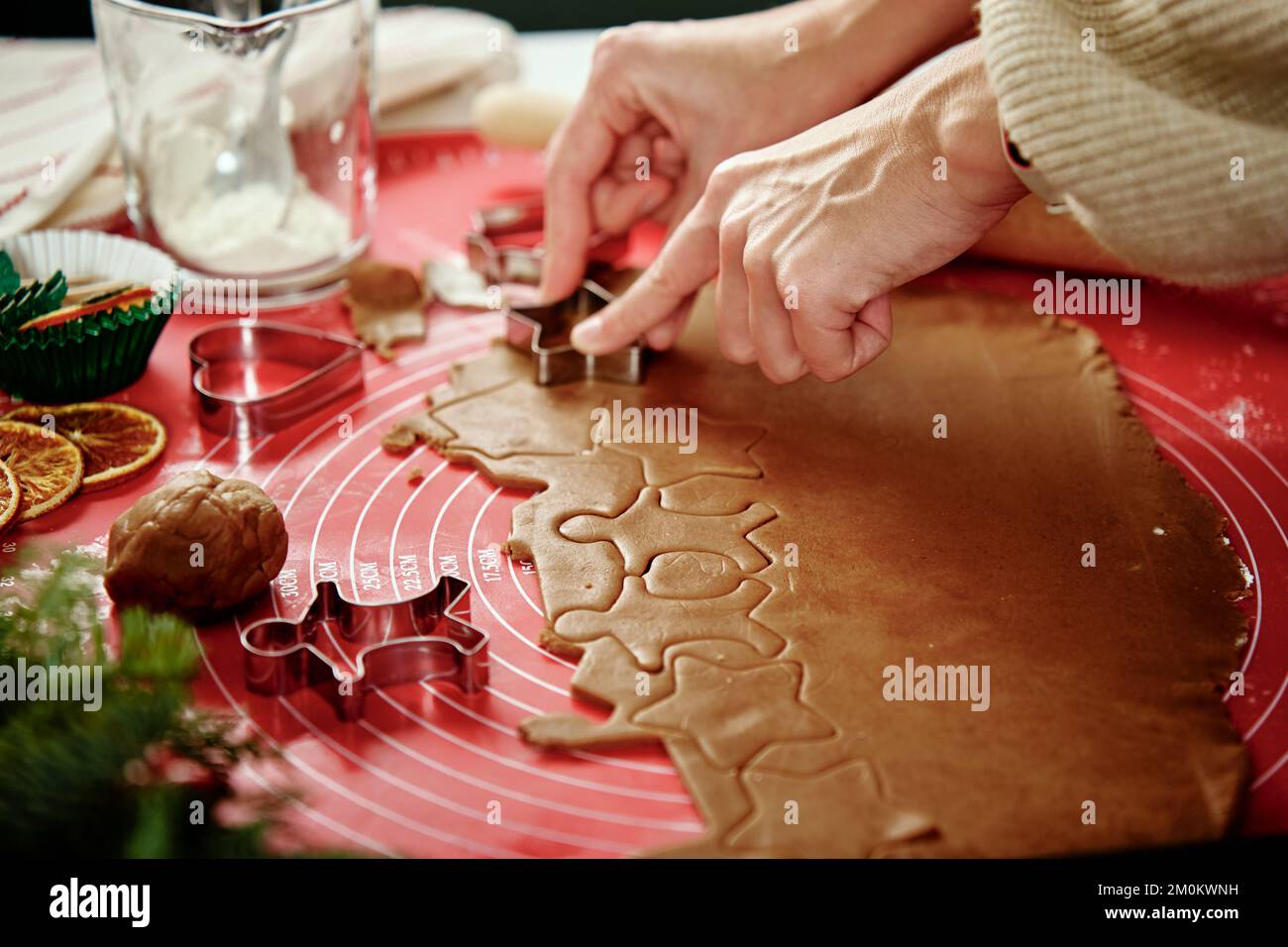 Woman preparing gingerbread cookies at kitchen with Christmas decorations. Female hands cutting ginger dough with cutter to making cookies for winter Stock Photo