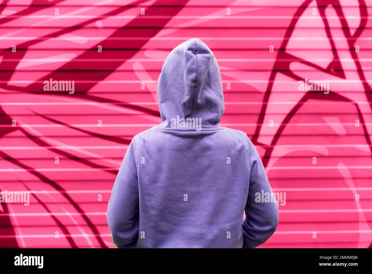 Young woman in hood in purple violet hoodie from back on pink red abstract modern background viva magenta color and very peri copy space mockup friend Stock Photo
