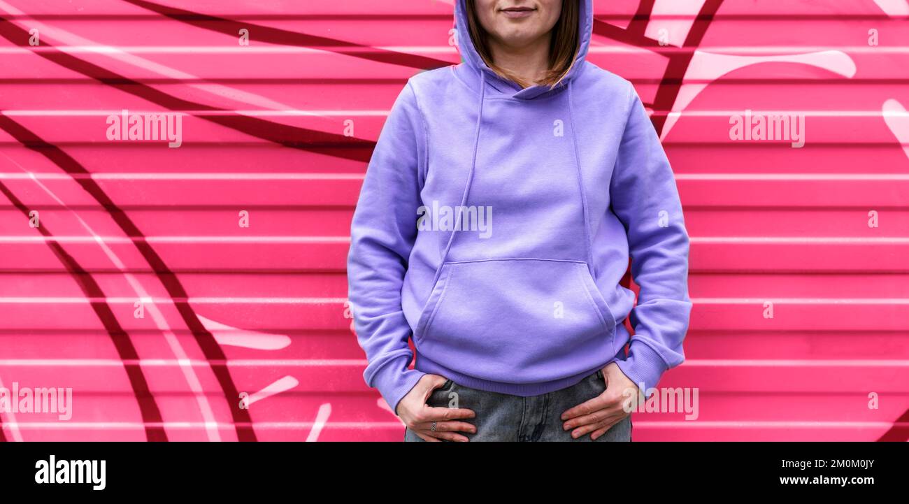 smiling Young woman in hood in purple violet hoodie from back on pink red abstract modern background viva magenta color and very peri copy space mocku Stock Photo