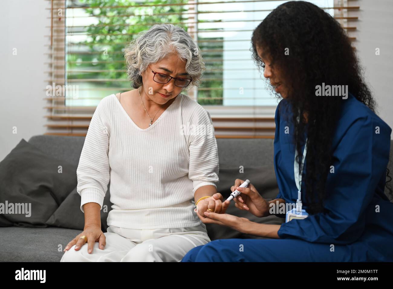 Female caregiver measuring glucose level of diabetic senior woman