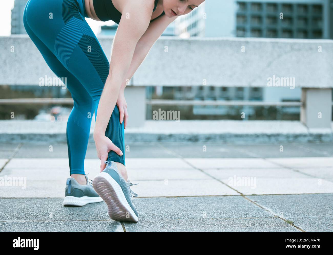 Closeup of one caucasian woman holding her sore ankle while exercising outdoors. Female athlete suffering with painful foot injury from fractured Stock Photo