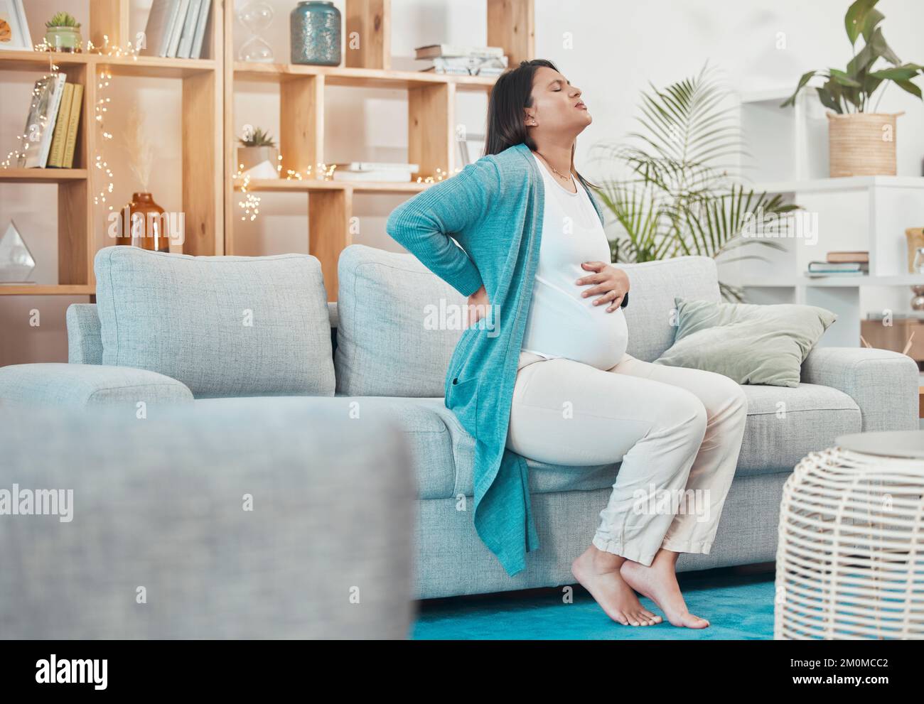 Pregnant, woman and back pain with a mother feeling painful body while sitting on her couch