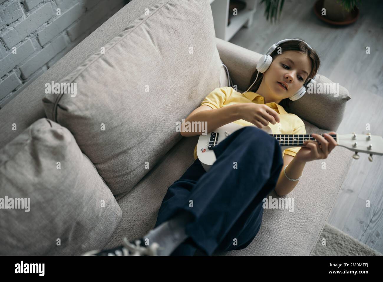 top view of girl playing ukulele while lying on couch in wired
