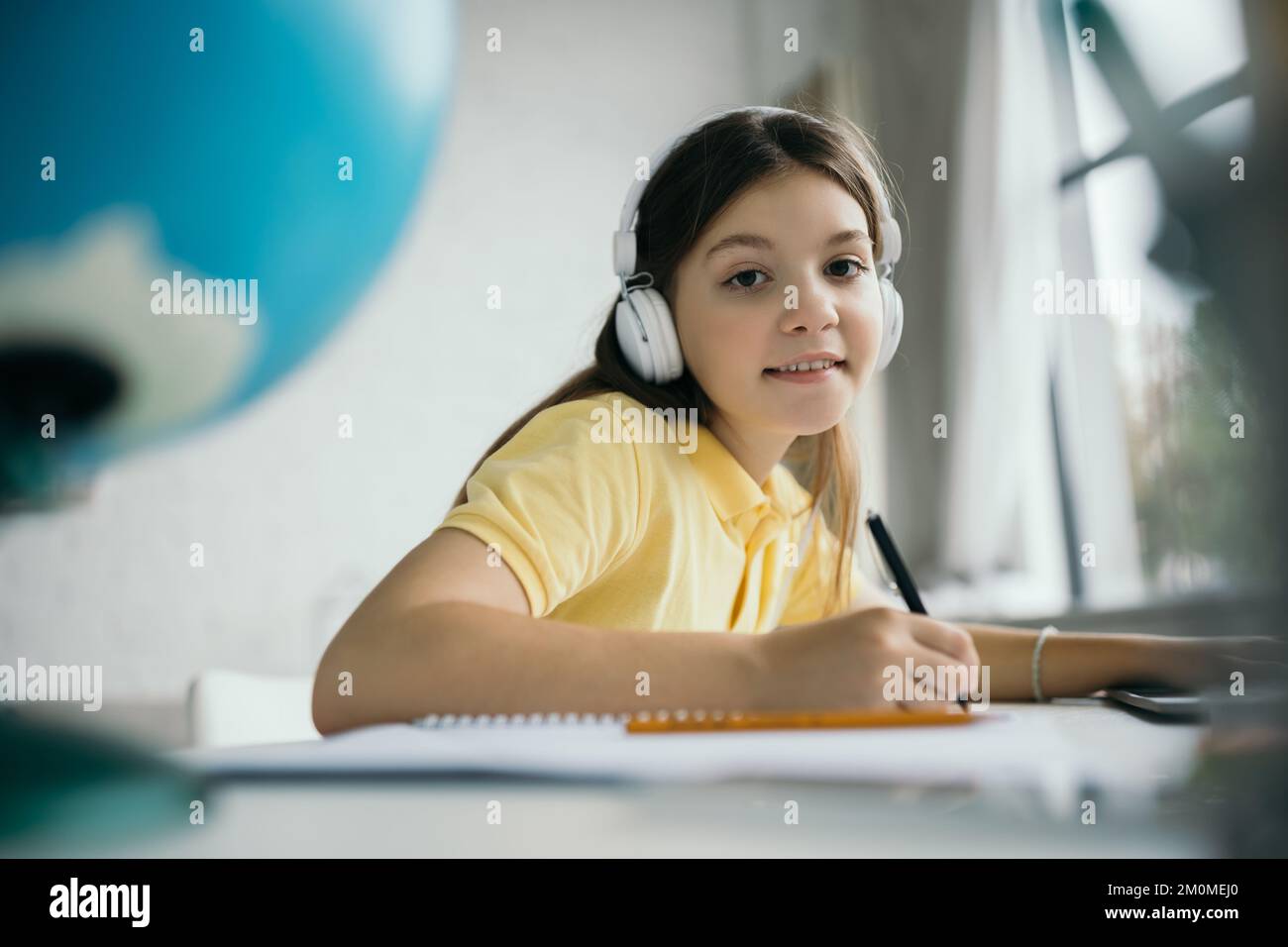 happy preteen girl in headphones doing homework and smiling at camera ...