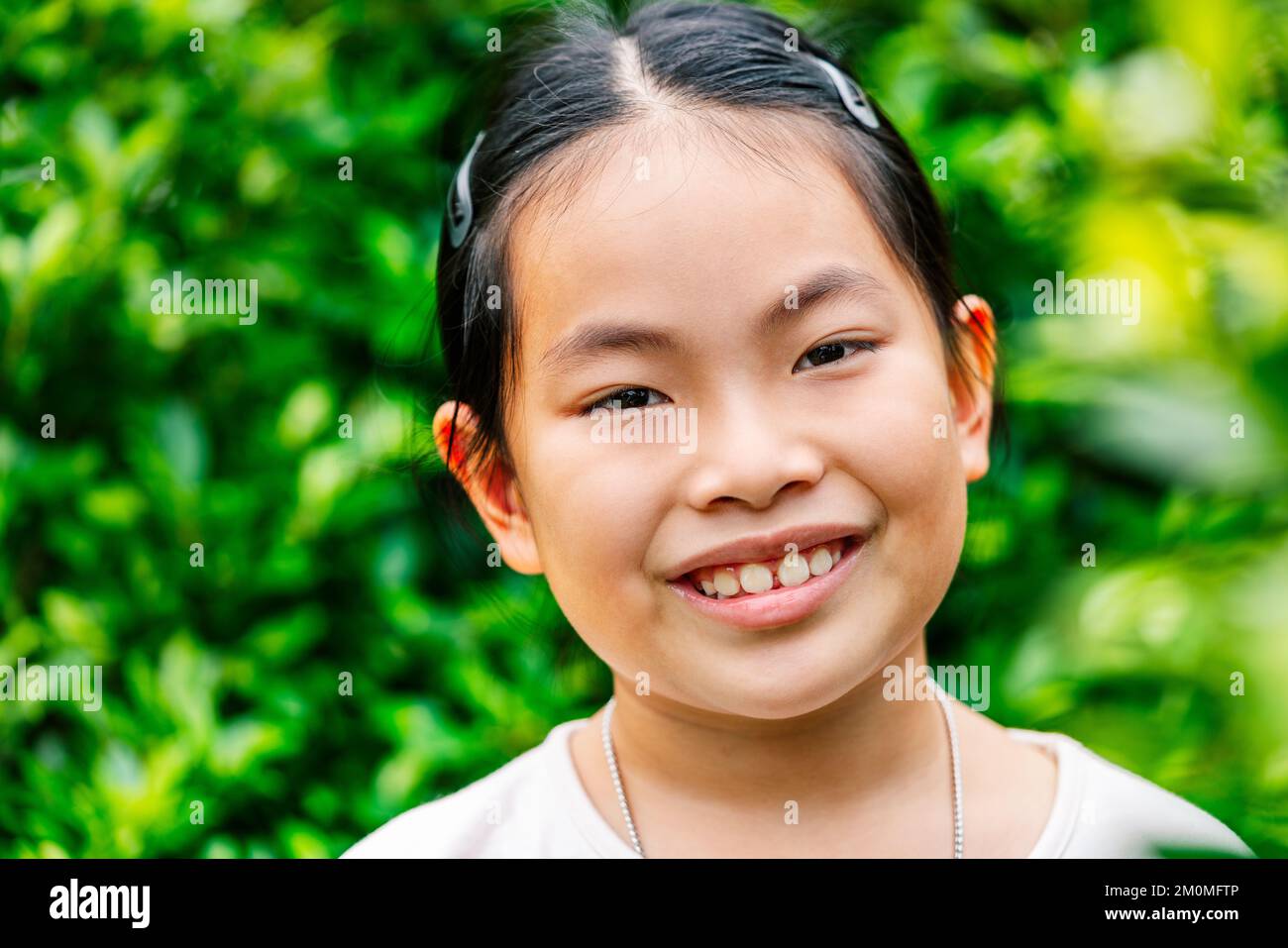 Portrait of cute and healthy Asian child girl in 8 to 9 years old, close up to face, smiling, looking at camera, outdoor image, blurred background of Stock Photo