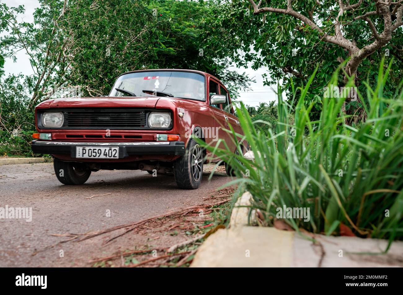 An old red Moskvitch Russian car moving through a road with a lot of ...