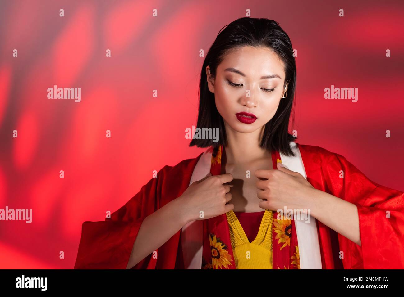 young asian woman in kimono cape touching neckerchief with floral print on abstract background with red gradient,stock image Stock Photo