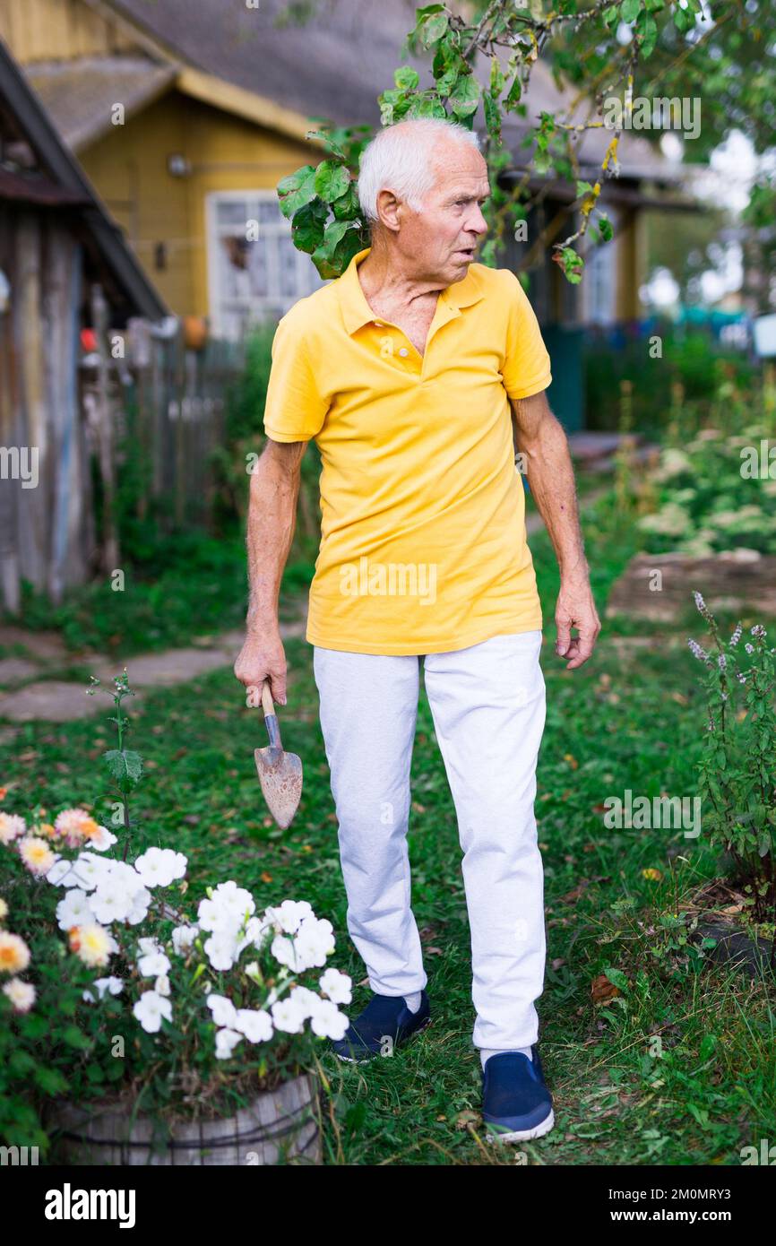 Skilled elderly worker caring for flowers in summer garden Stock Photo