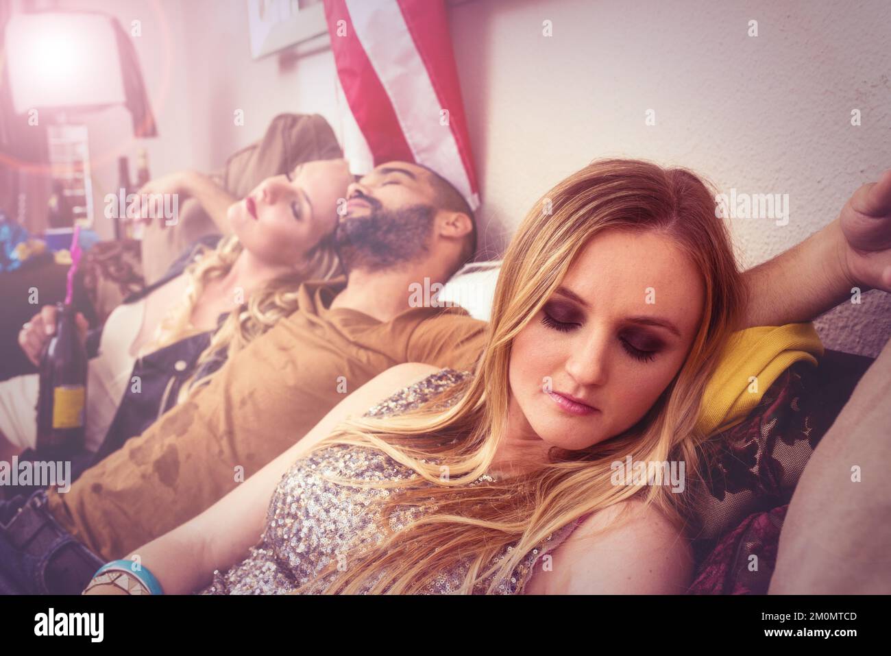Drunk, sleeping and real people at a party on a sofa with a hangover from a celebration at a house. Tired, alcoholic and young man taking a nap with Stock Photo