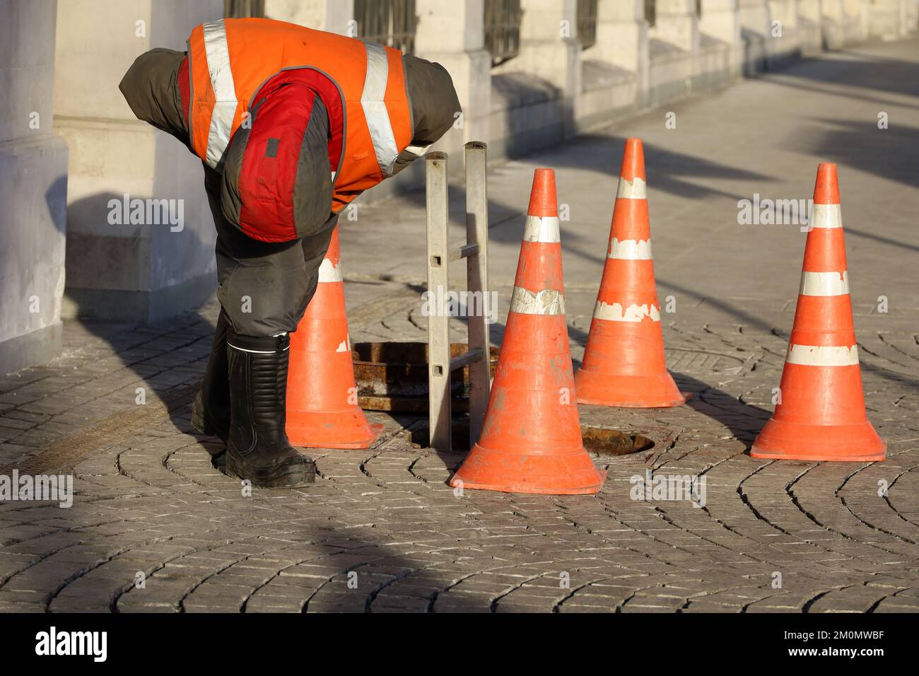 Worker standing over the open sewer hatch on winter street. Concept of repair of sewage, underground utilities, cable laying Stock Photo