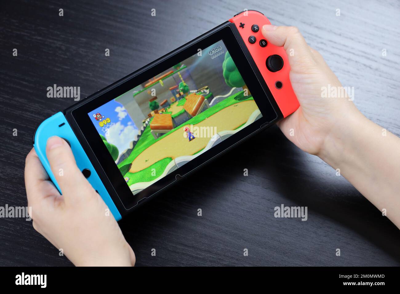 Defocused view to girl playing Super Mario Odyssey game on Nintendo Switch console in handheld mode Stock Photo