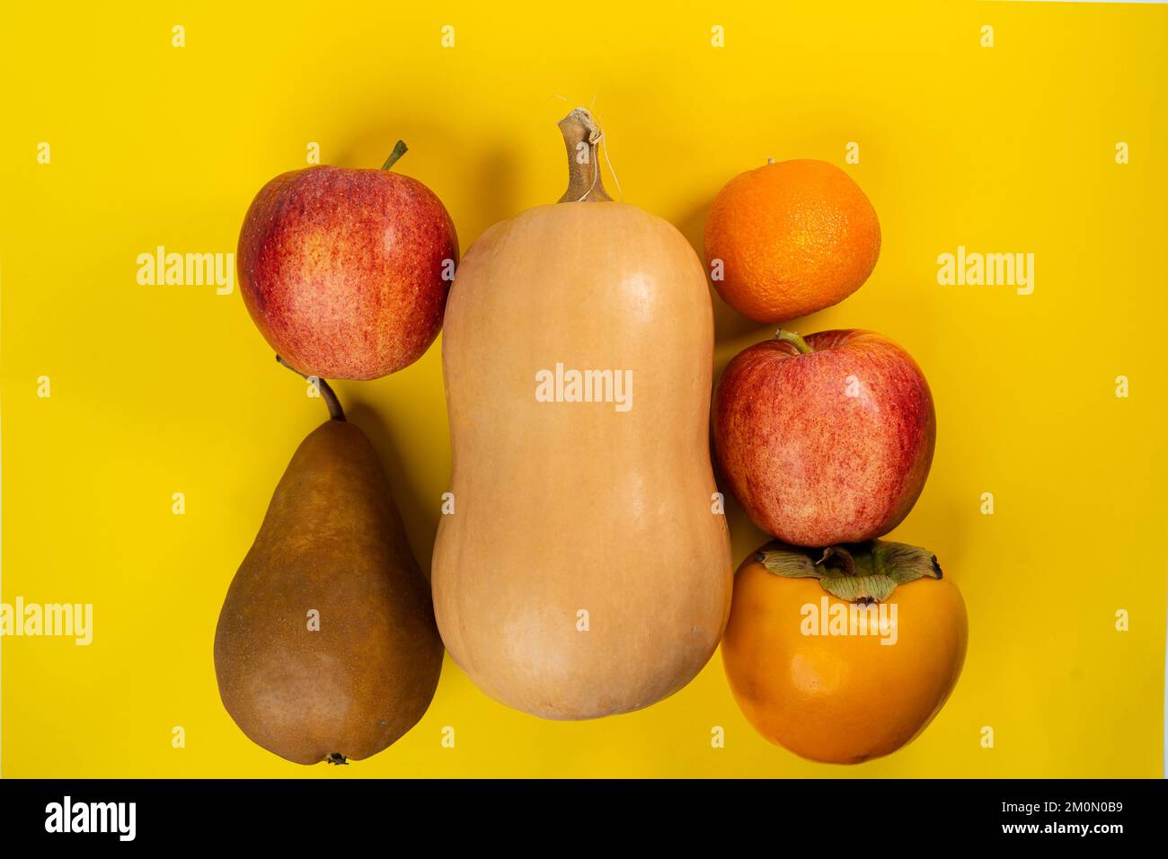 Pumpkin, apple, pear, tangerine and persimmon on a yellow background Stock Photo