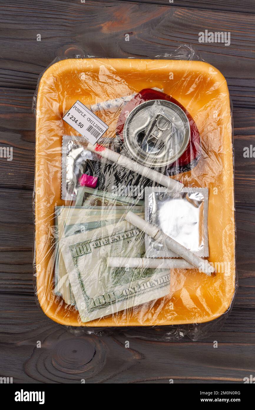 Top view teenage stuff wrapped in plastic. Money with condom and cigarettes. Stock Photo