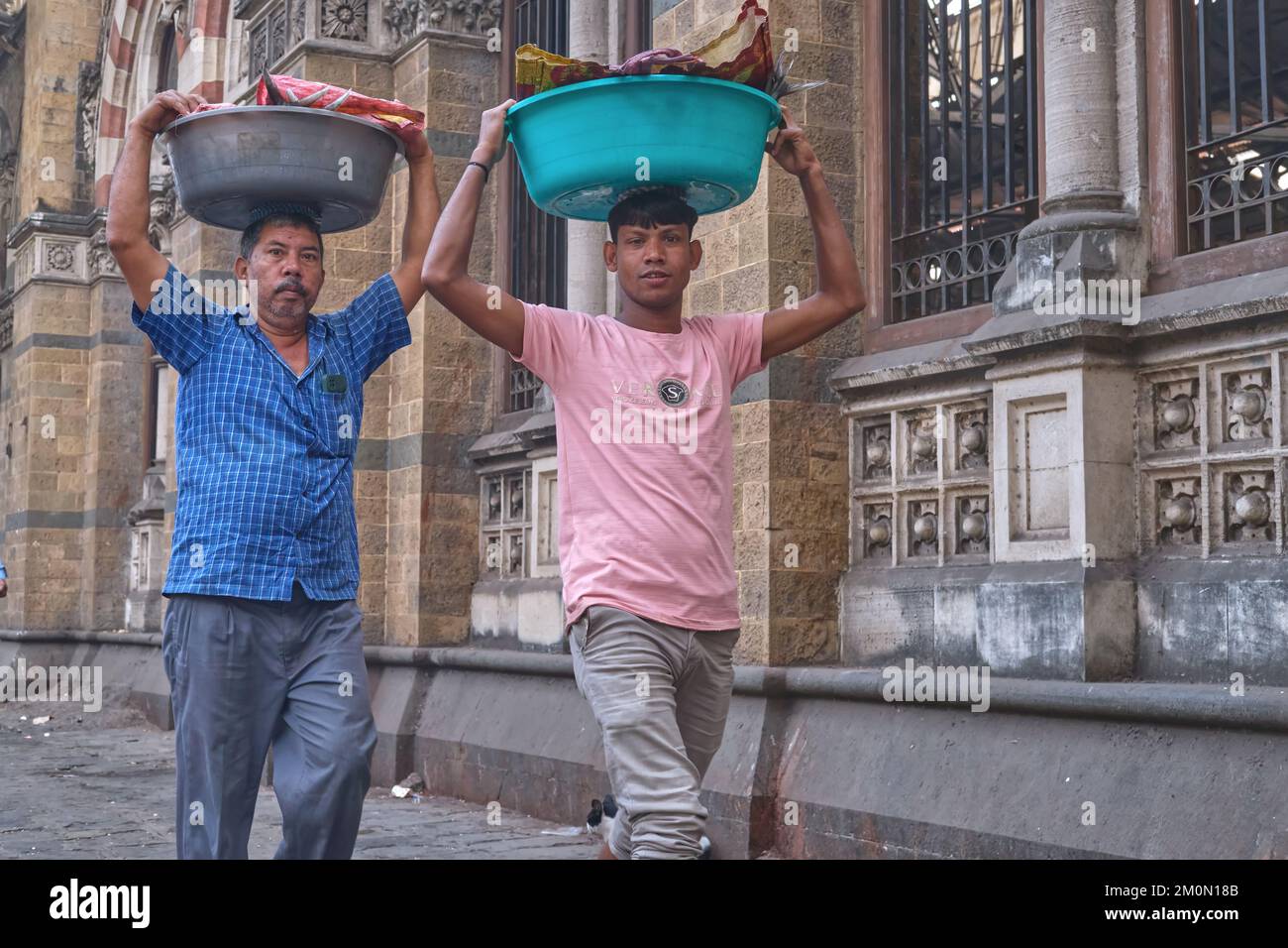 Two porters with trays of fish on their heads, outside Chhatrapati Shivaji Maharaj Terminus (CMST), in Mumbai, India, to forward the trays by train Stock Photo