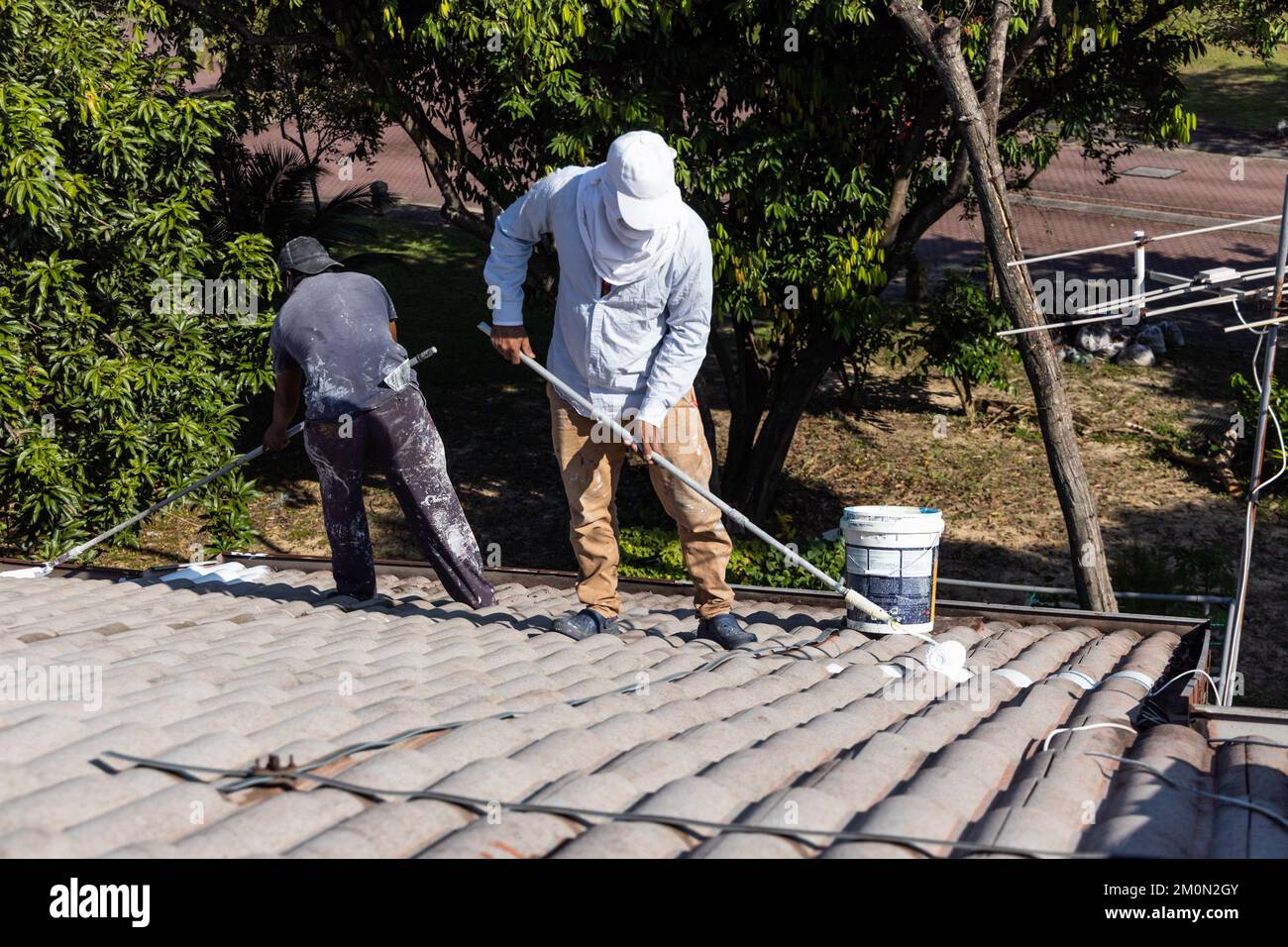Worker adding undercoat foundation paint onto rooftop with roller at
