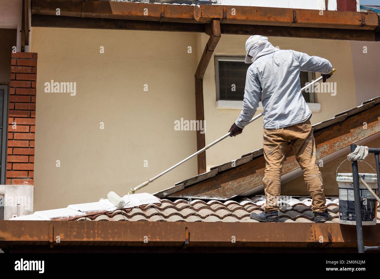 Worker adding undercoat foundation paint onto rooftop with roller at
