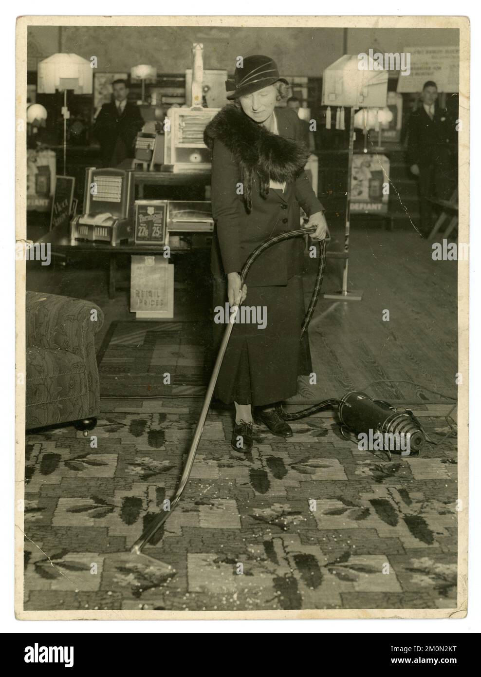 Original 1930's era press release from an electrical household goods showroom, maybe in-store demonstration in a department store, by smartly dressed woman demonstrator -  staff or customer, demonstrating using a vacuum cleaner in U.K. furniture shop showroom, early labour saving housework device, UK circa.1933. Stock Photo