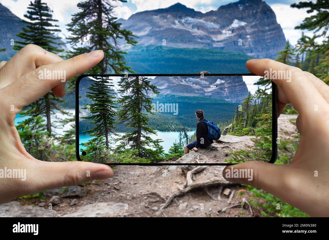 Tourist taking a picture with a mobile phone of a man resting at the lake Ohara, Canada. Stock Photo