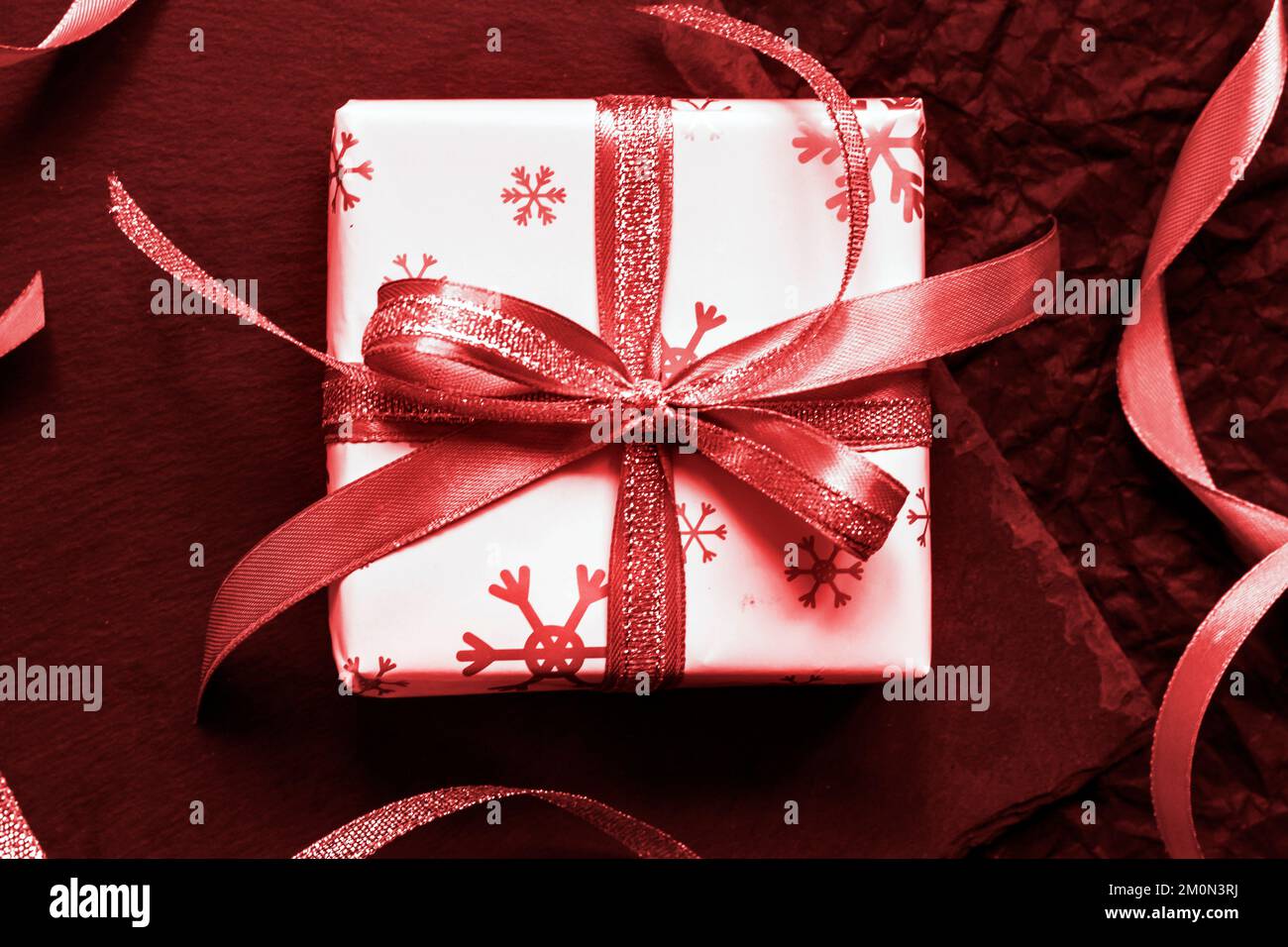 Christmas gift box wrapped in a white paper with snowflakes and tied with a ribbon. Red toned. Flat lay, top view Stock Photo