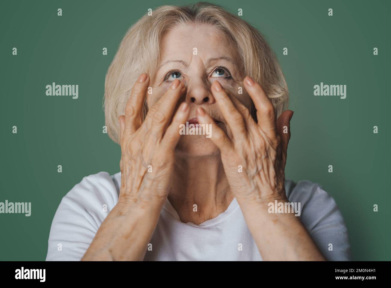 Portrait of pretty senior woman with hydrogel under-eye patches in the morning, showing an effect of perfect skin, isolated on green background. Anti Stock Photo