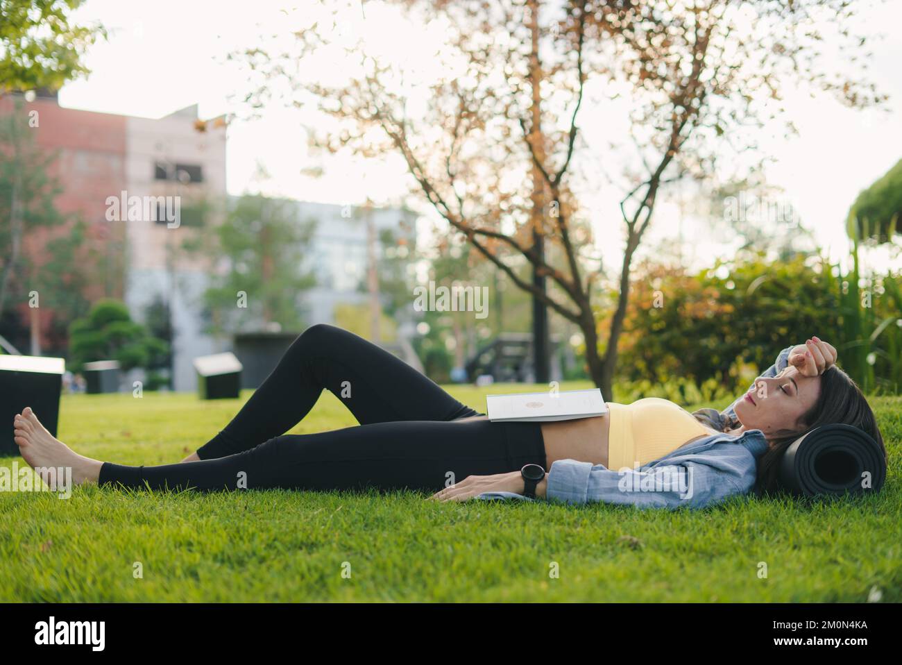 Side view of a sporty girl resting and reading an interesting book, outdoors in city park. Beautiful green. Fitness woman. Nature summer. Summer Stock Photo