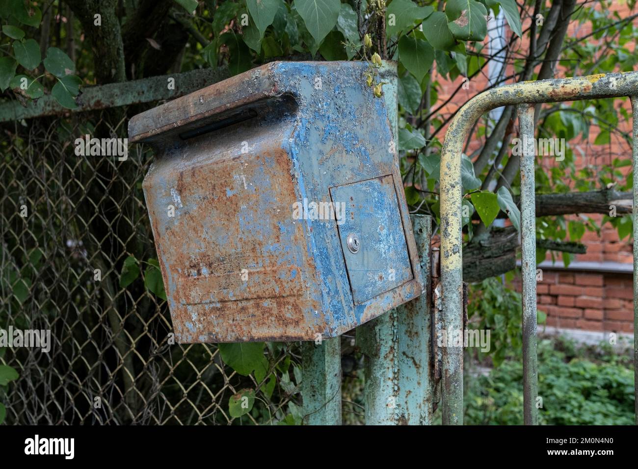 Mailbox is hanging on the fence. Old, rusty mailbox with peeling paint. Stock Photo
