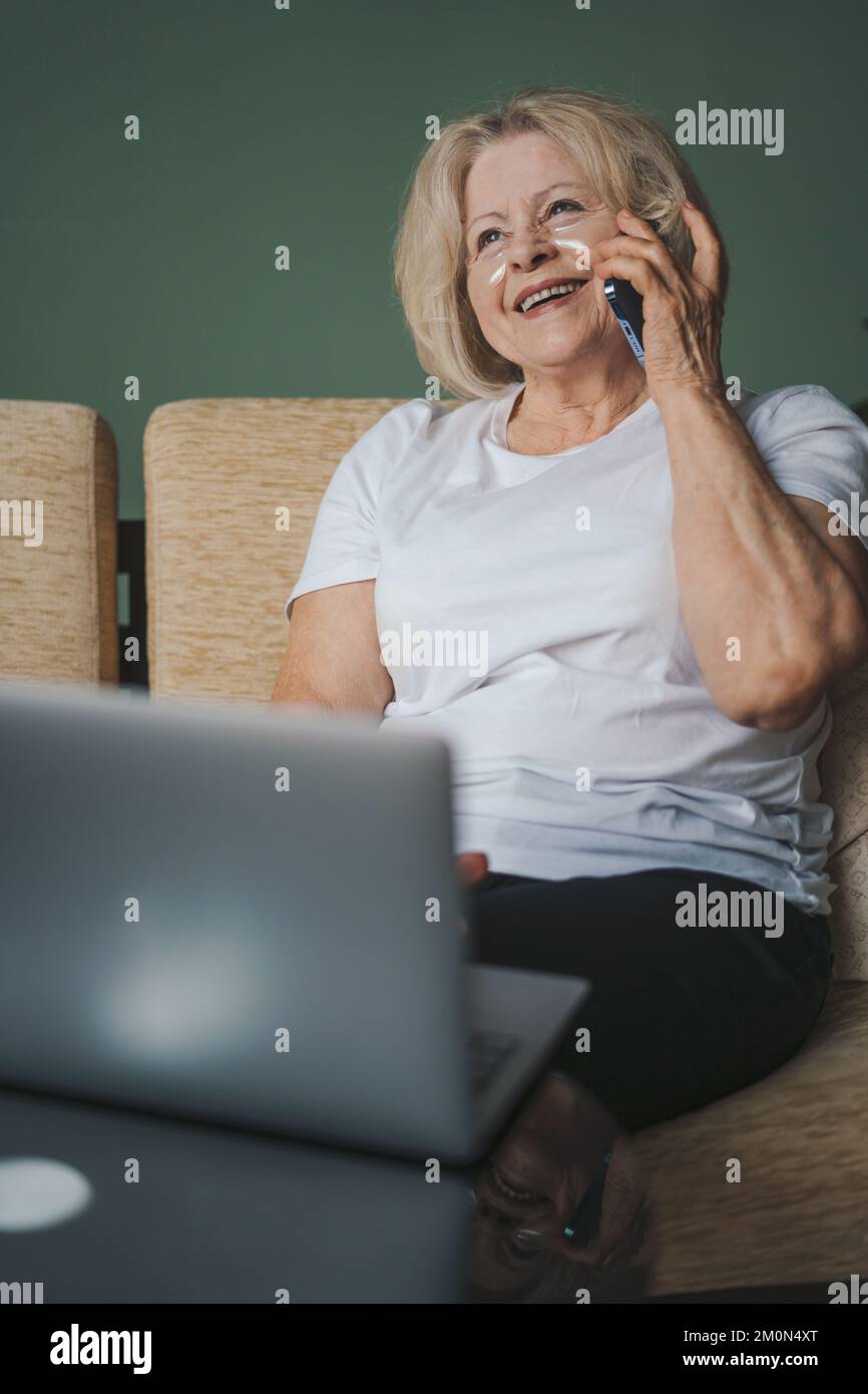 Happy old mature retired woman relaxing alone on cozy sofa, enjoying a conversation on her mobile phone spending weekend time alone at home. Elderly Stock Photo