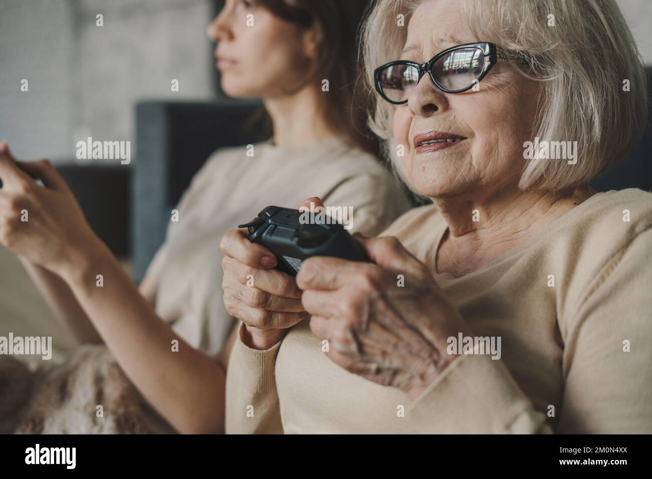 Happy senior mother with daughter using joysticks together, having fun playing video-games. Family home leisure. Happy family. Stock Photo
