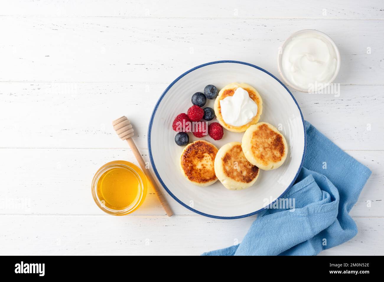 Sweet curd cheese or cottage cheese fritters aka syrniki served with sour cream, berries and honey. Top view, copy space Stock Photo