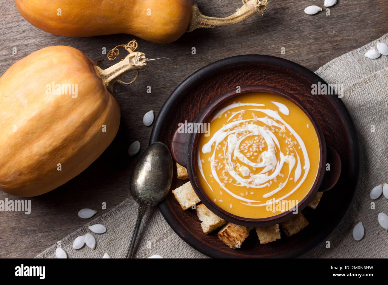 Pumpkin soup with cream and sesame seeds in brown ceramic bowl on wooden background. Flat lay, top view. Stock Photo