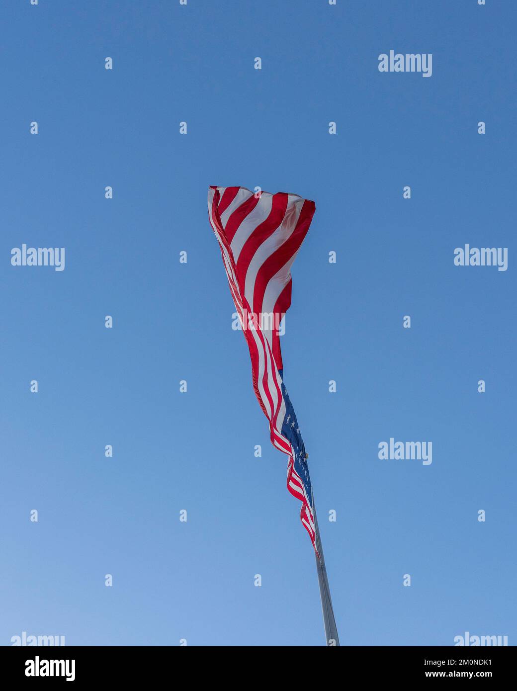 A large American flag blows in the wind against a bright blue sky. Stock Photo