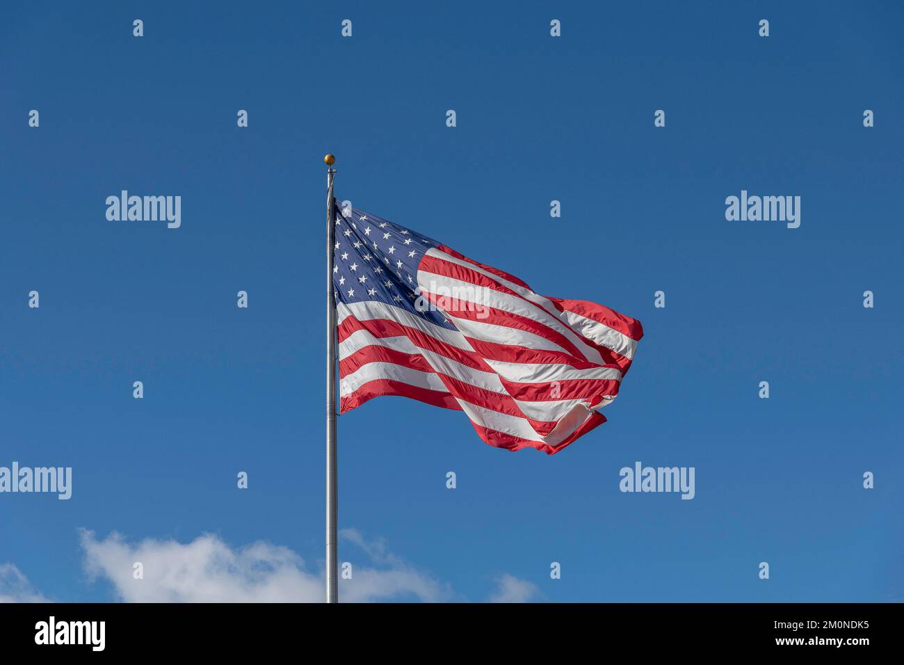 A large American flag blows in the wind against a bright blue sky. Stock Photo