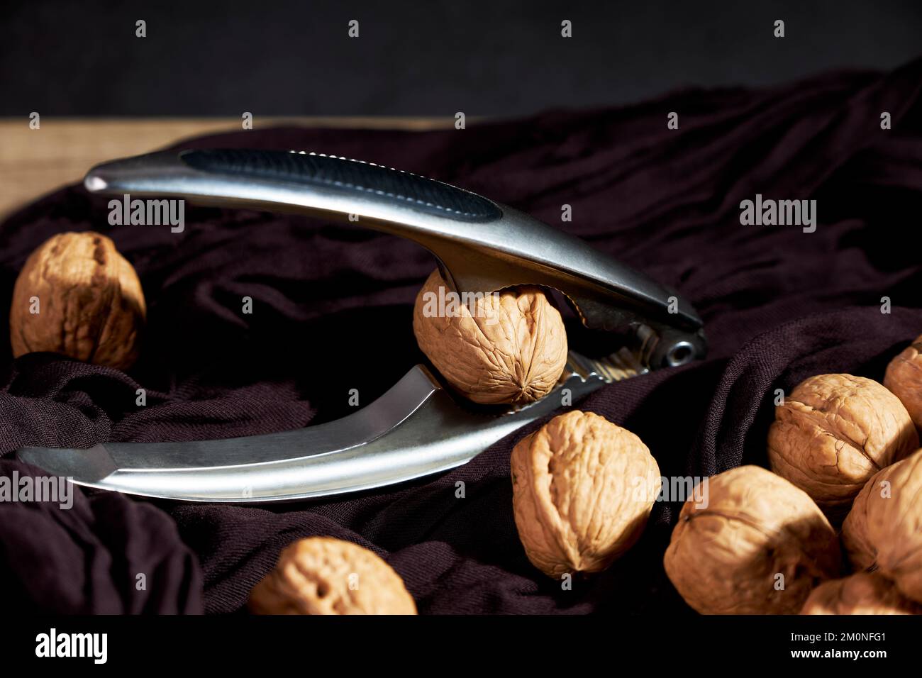 Close-up of tasty nuts with a metal nutcracker on wooden table. Healthy food Stock Photo