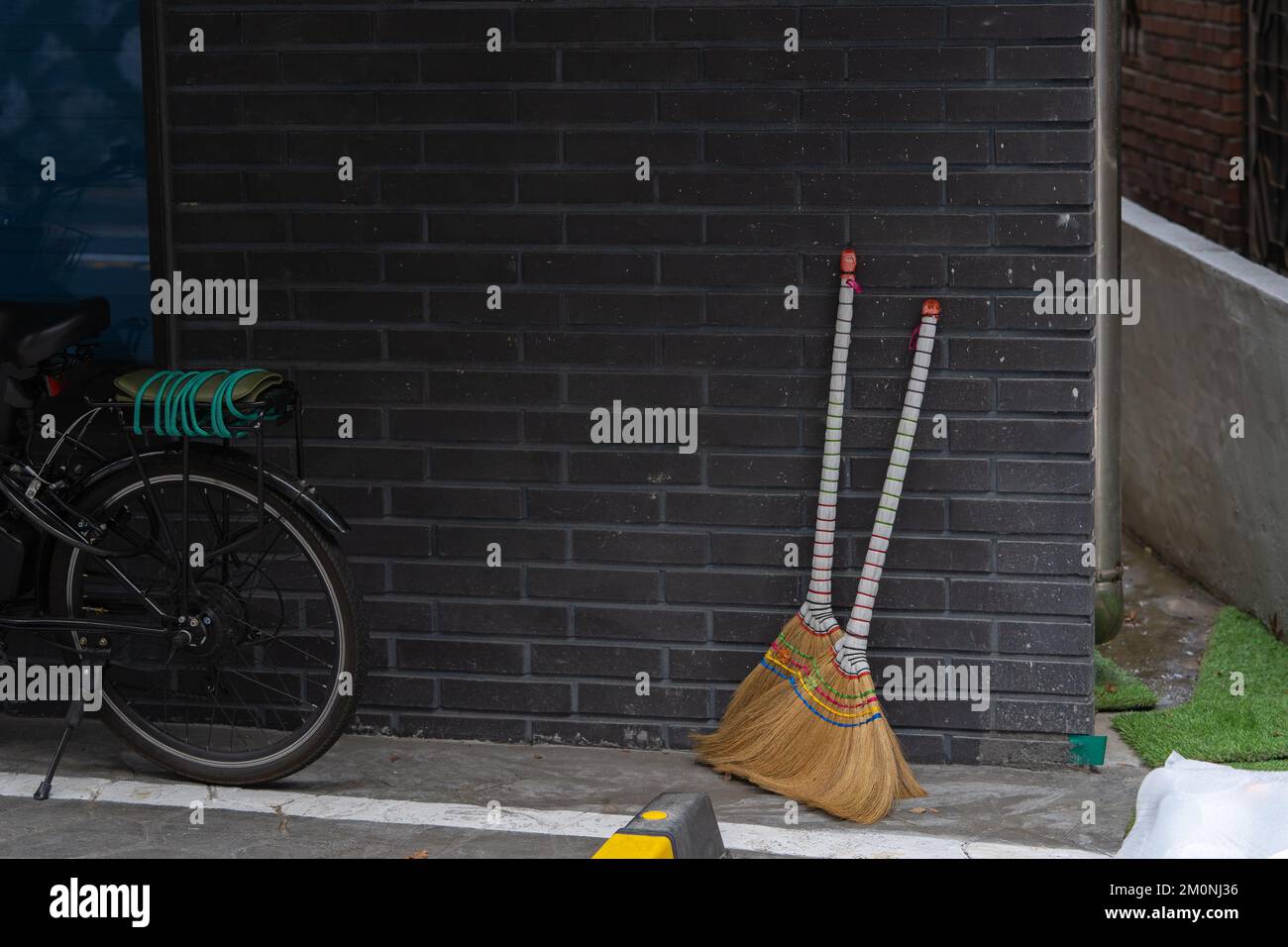 Two straw brooms decorated with colored thread are propped up against