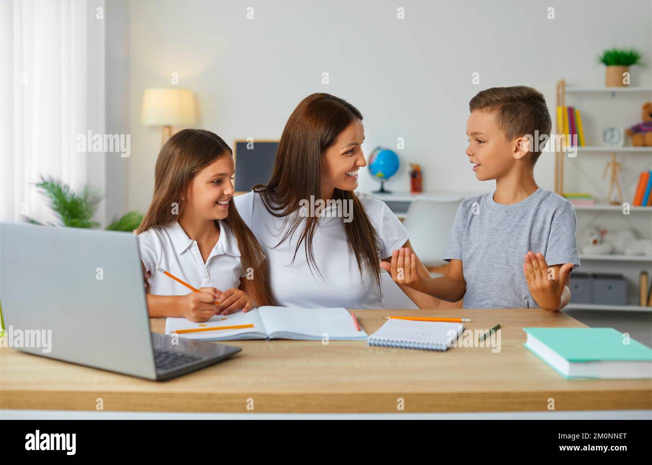 Caring and friendly young mother helps her children to complete their school homework. Stock Photo