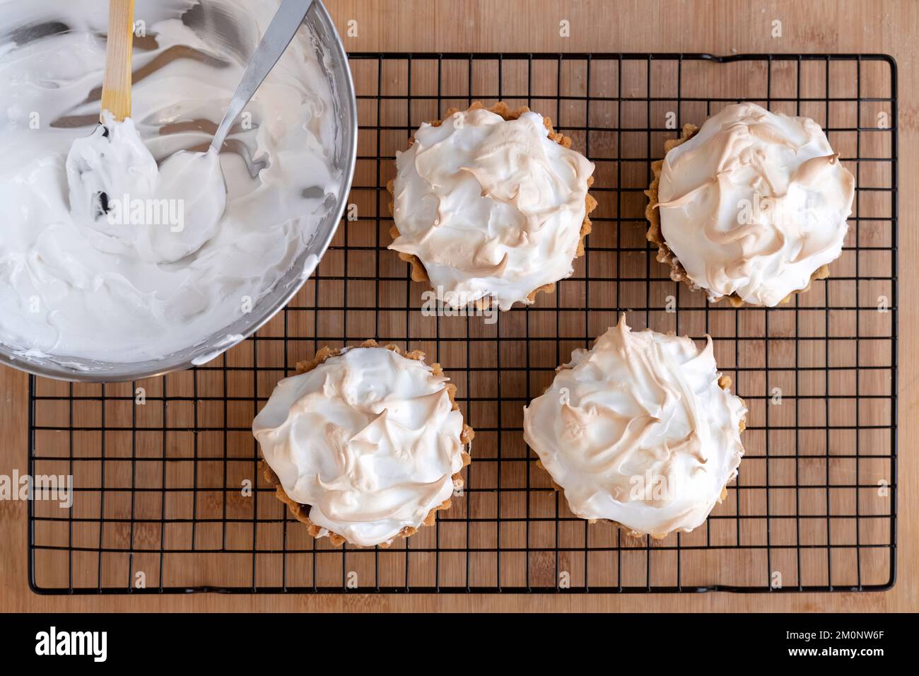 Freshly home baked marzipan mince tartlets or pies topped with meringue cooling on a cake rack having just been taken out of the oven Stock Photo