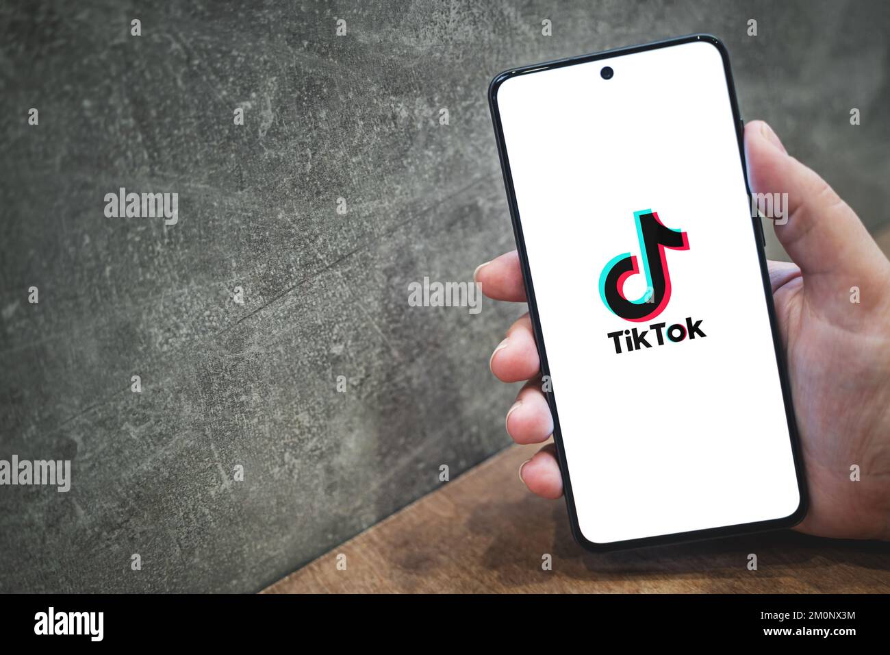 Tik tok application logo on smartphone screen in hand, concrete background with copy space for text. Tiktok social media app icon. Krakow, Poland - November 11, 2022. Stock Photo