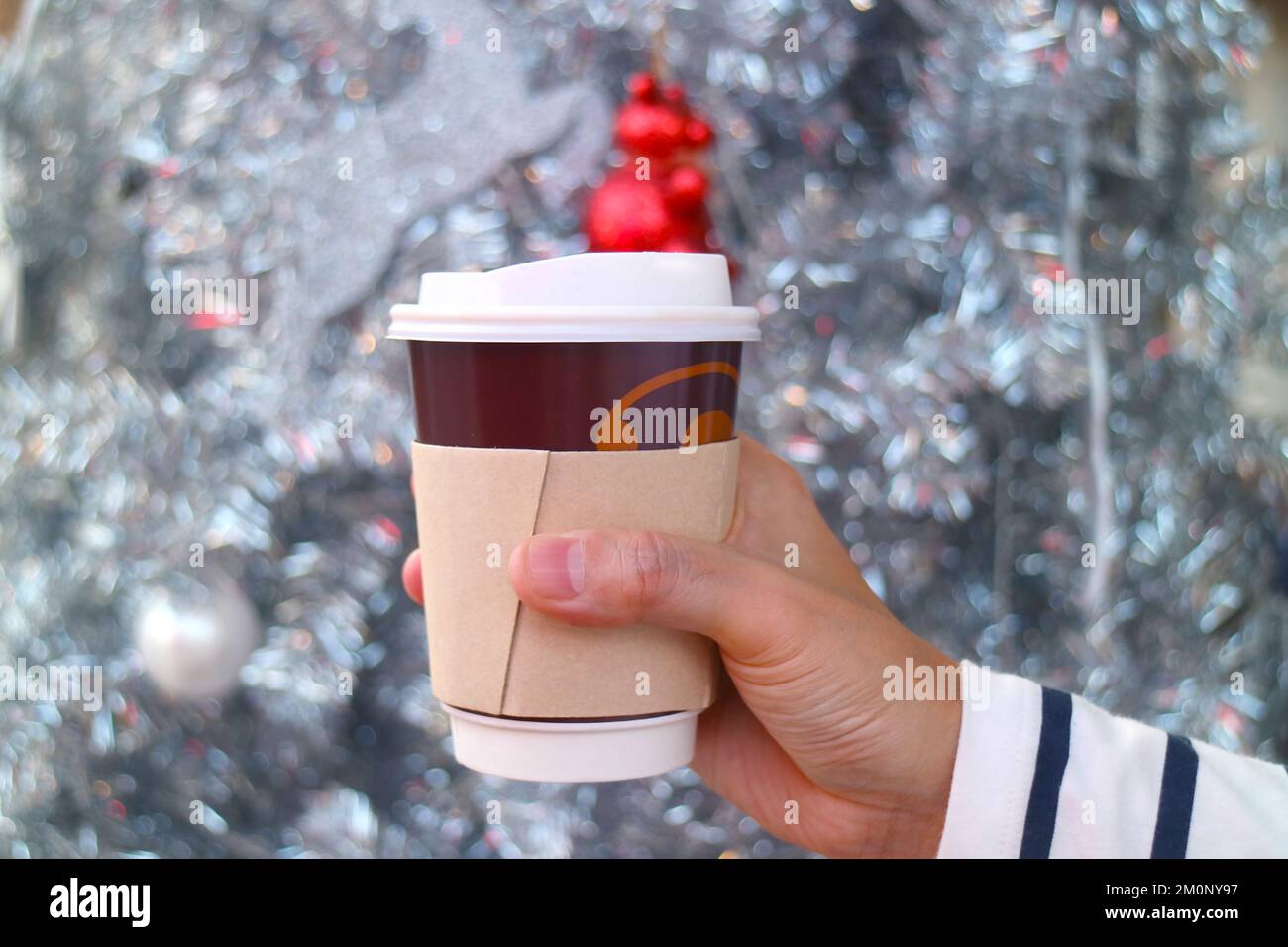 Hand Holding Takeaway Coffee Cup with Blurry Glittering Christmas Tree in Background Stock Photo