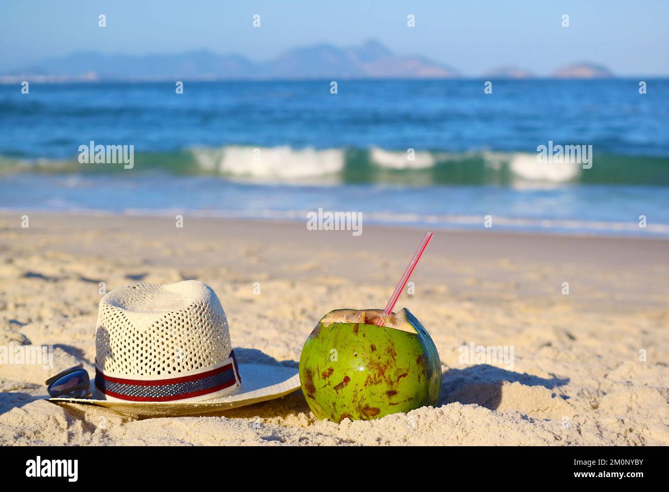 Fresh young coconut with Straw hat and sunglasses on the sandy beach of Copacabana, Rio de Janeiro, Brazil, South America Stock Photo