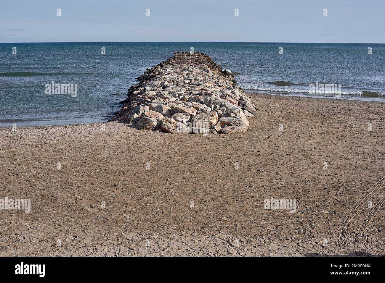 Rock breakwater entering into the blue sea.Blue sky, calm sea, empty