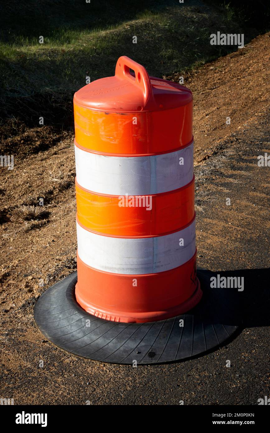 Vertical shot of a single orange and white traffic barrel in late afternoon sunlight. Stock Photo